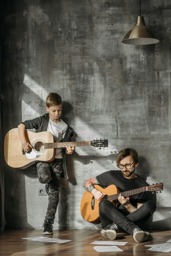 pexels-photo-7521074-7521074 A father and son share a musical moment, playing guitars indoors with warm lighting.